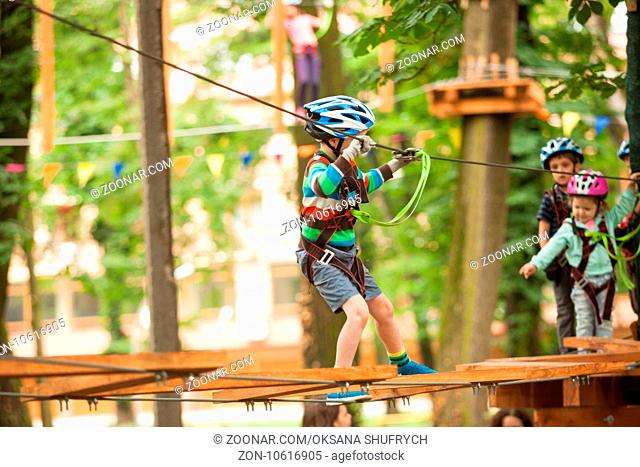 A boy in a helmet and safety equipment in adventure ropes park on the background of nature