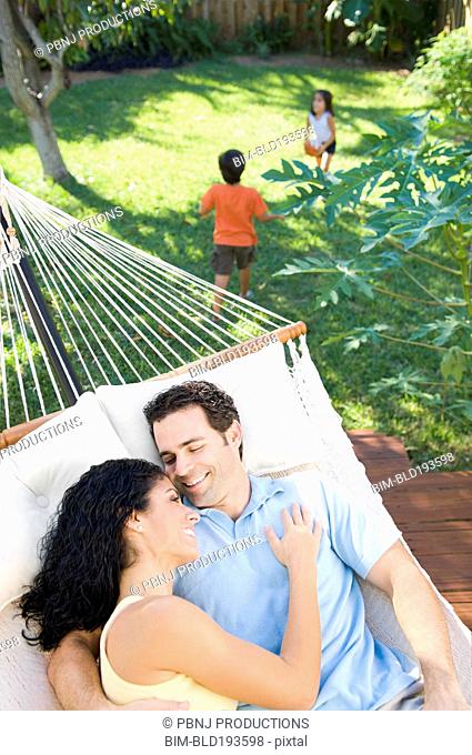 Couple relaxing in hammock with children playing in background