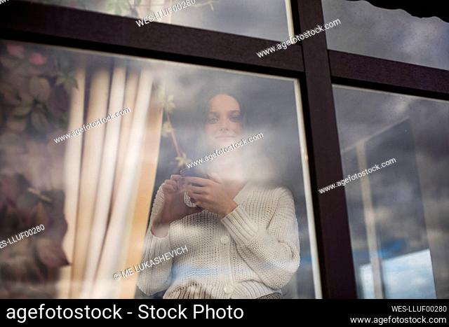 Young woman with coffee cup behind window