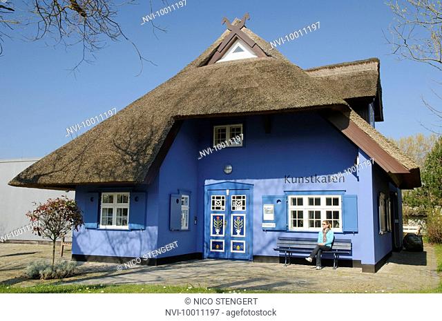 Tourist sitting in front of Kunstkaten art gallery with a traditional thatched-roof, Ahrenshoop seaside resort, Mecklenburg-Western Pomerania, Germany, Europe