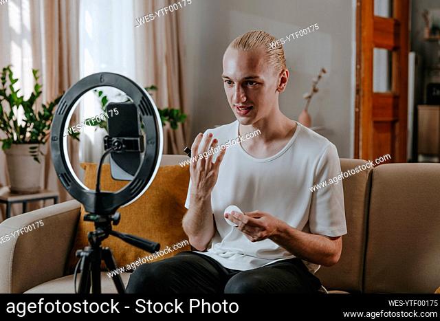 Young make-up artist vlogging through smart phone in front of ring light at home