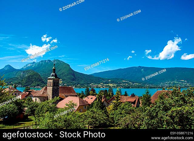 View of houses and belfry with blue sky mountains landscape on background, in the village of Talloires. A lovely village next to the Lake of Annecy