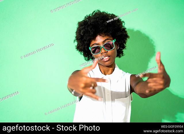 Woman wearing sunglasses gesturing while standing against green background