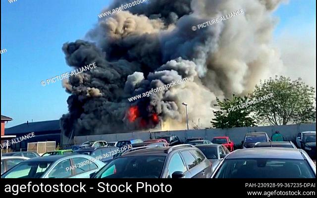 28 September 2023, Lower Saxony, Neustadt am Rübenberge: Flames and clouds of smoke rise from a warehouse. The burning warehouse of a painting company has...