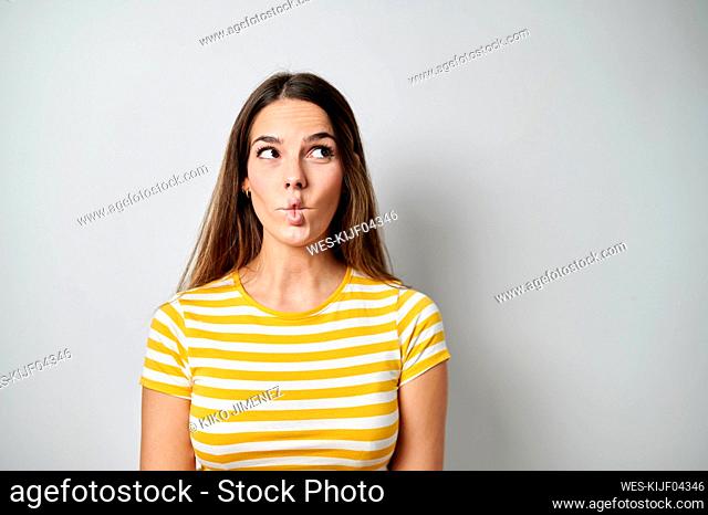 Thoughtful woman puckering on gray background