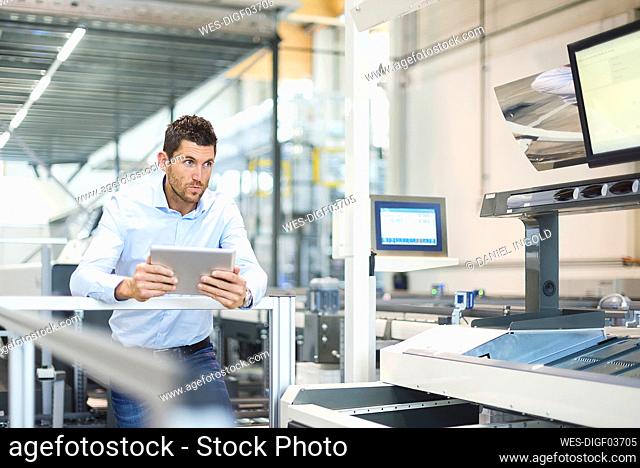 Businessman with tablet looking at machine in modern factory