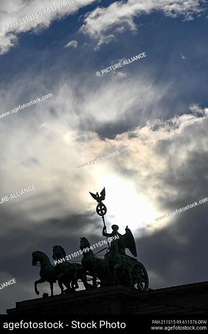 15 October 2021, Berlin: Behind many dark clouds and a little blue sky, the sun can be seen temporarily behind the Quadriga on the Brandenburg Gate