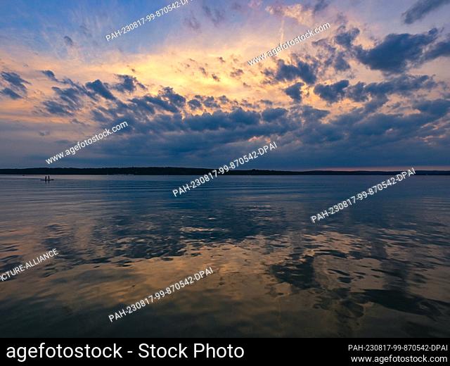 17 August 2023, Brandenburg, Diensdorf-Radlow: Two people are on stand-up paddle boards in the evening on the Scharmützelsee