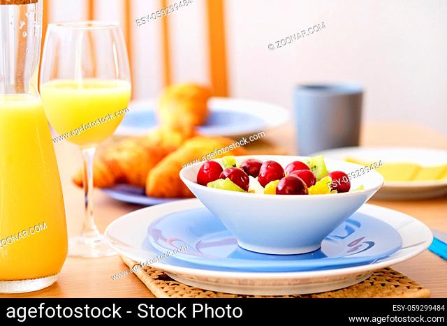 Close up fresh healthy nutritious breakfast jug glass with orange natural juice croissants on background, bowl plate with porridge or cereals garnished cherry