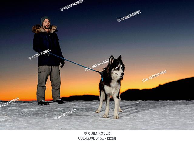 Mature man standing with dog in snow at night