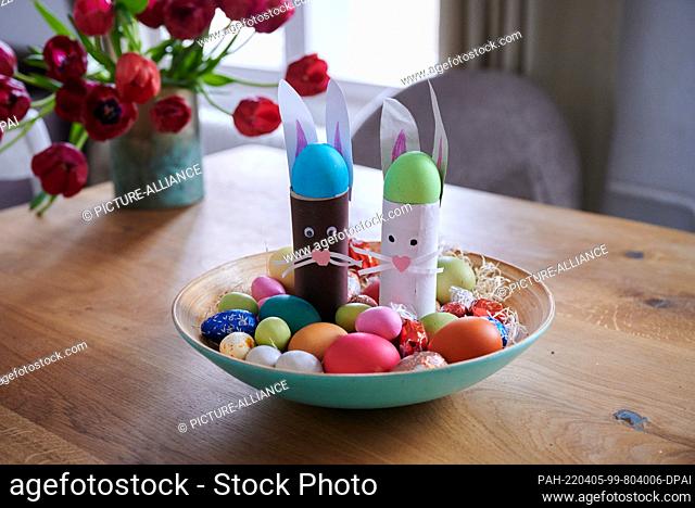 PRODUCTION - 31 March 2022, Berlin: ILLUSTRATION - An Easter nest with homemade bunnies, colored eggs and chocolate eggs lies in a bowl on a table