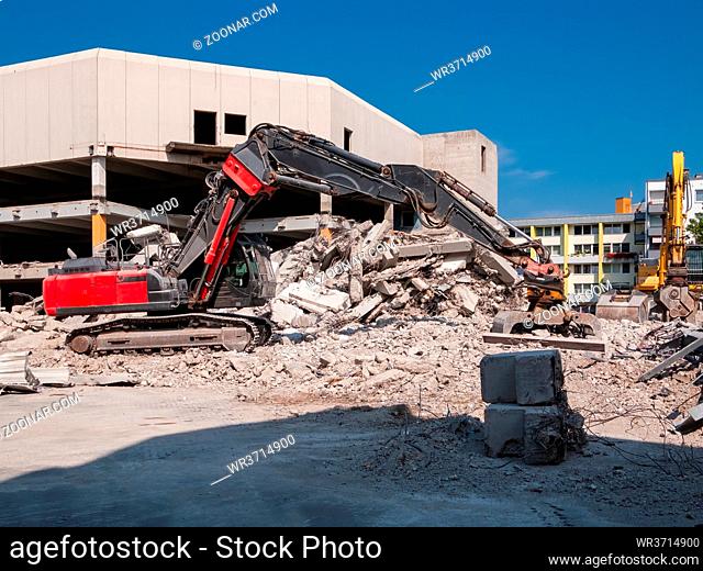 Roter Abrissbagger mit Greifer vor Abbruchgebäude