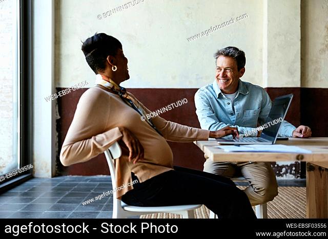 Happy businessman sitting with colleague at desk