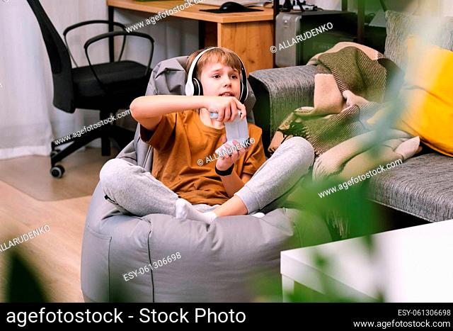 Boy teenager playing video game with joystick sitting on frameless beanbag chair at home