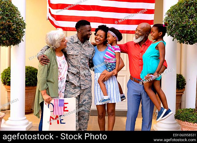 Cheerful african american family standing together with placard against usa flag at house entrance