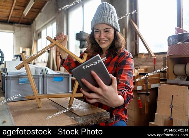 Smiling carpenter holding tablet and workpiece in her workshop