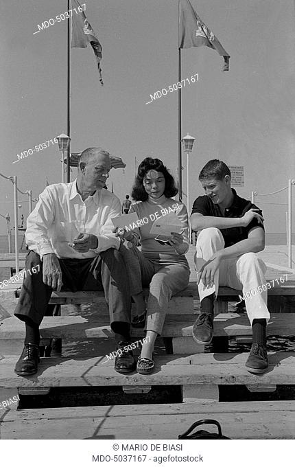 American writer Erskine Caldwell reading a letter on a beach of the Lido with his fourth wife Virginia and his son Jay born from a previous marriage