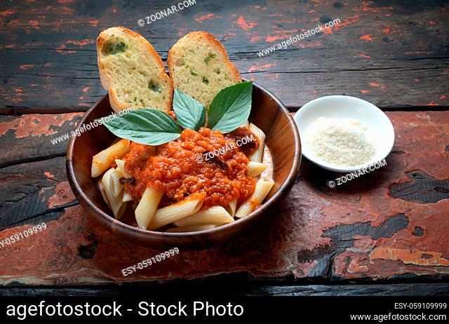 Pasta with tomato sauce, garlic bread and parmesan cheese aside isolated on rustic wooden background
