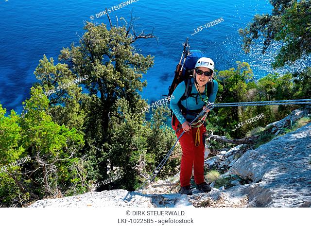A young woman with trekking gear abseiling in the mountainous coastal landscape above the sea, Golfo di Orosei, Selvaggio Blu, Sardinia, Italy, Europe