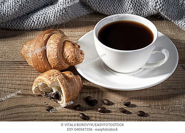 Black coffee with croissants. Coffee grains on a wooden table. Knitted woolen scarf in the background
