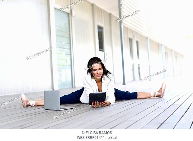 Female balett dancer sitting on the ground, using tablet and laptop
