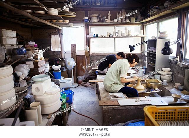 Woman working in a Japanese porcelain workshop, sitting at a potter's wheel, throwing bowl