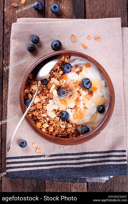 Homemade granola with nuts, candied oranges, fresh blueberries and yogurt in a wooden bowl on a wooden background