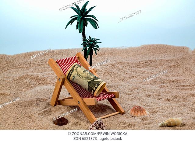 Liegestuhl mit Dollar am Sandstrand. Symbolfoto für Kosten bei Reise, Urlaub, Ferien. Sparen im Urlaub