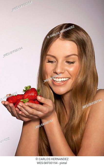 Young woman holding handfull of strawberries, smiling, close-up