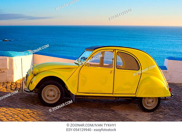 An Old yellow car in front of the ocean at sunset. Ericeira, Portugal