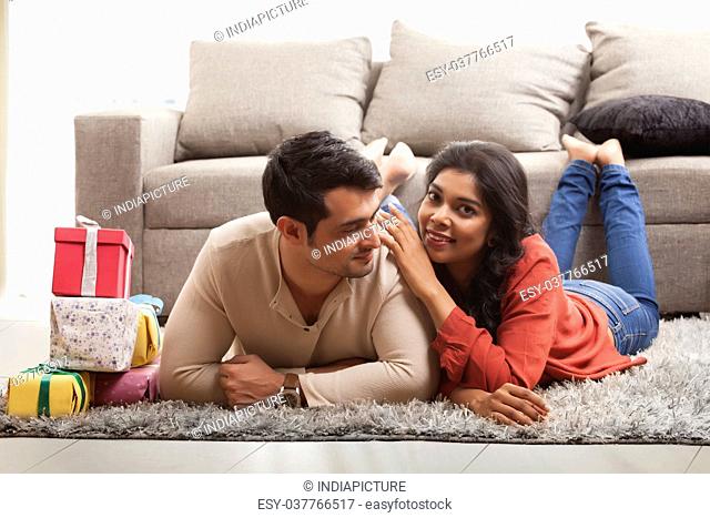 Young couple lying on carpet on the floor with gifts