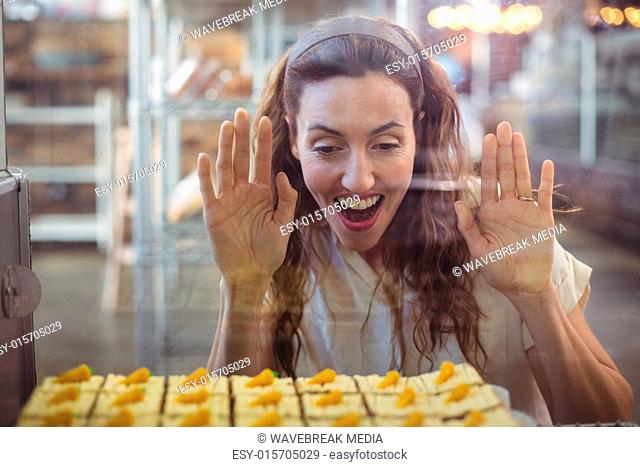 Pretty brunette looking at pastries through the glass