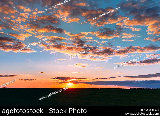 Natural Sunset Sunrise Over Field Meadow. Bright Dramatic Sky And Dark Ground. Countryside Landscape Under Scenic Colorful Sky At Sunset Dawn Sunrise