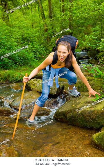 Young woman hiking through the woods and trying to cross a stream and accidentally falling into the water