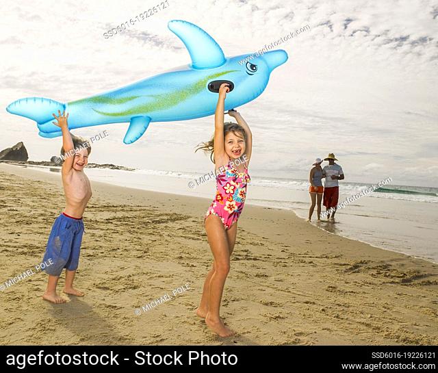Young children holding up inflatable dolphin and laughing at the beach