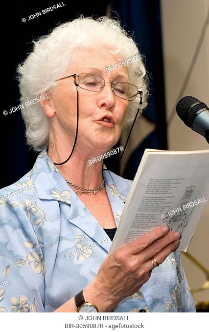 Elderly woman holding song sheet and singing into microphone