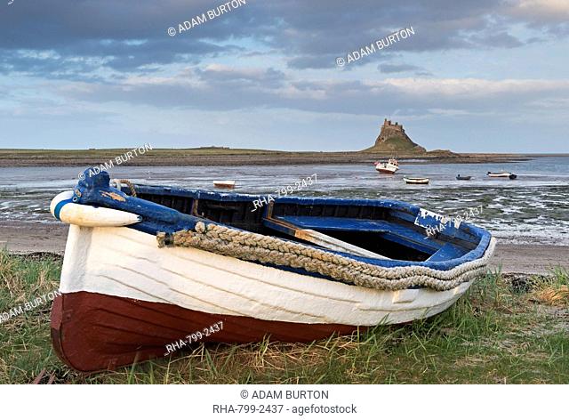 Fishing boat pulled onto the shore at Holy Island, looking towards the castle, Lindisfarne, Northumberland, England, United Kingdom, Europe