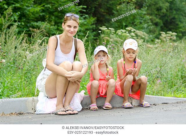 Mother and two children sitting on the curb of the road waiting for the bus