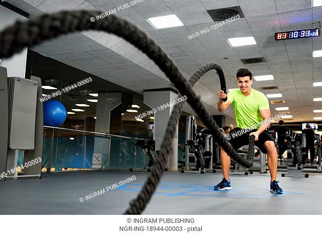 Man with battle ropes exercise in the fitness gym. Young male wearing sportswear