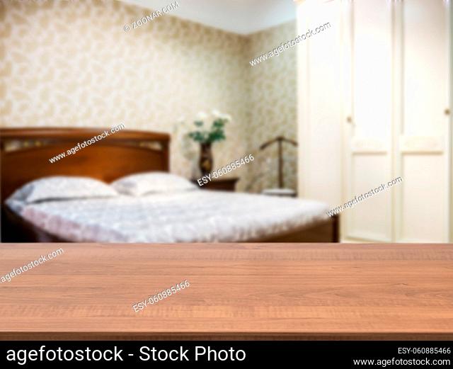 Wooden board empty table in front of blurred background. Perspective dark wood over blur in modern comfortable bedroom with dark brown wooden bed