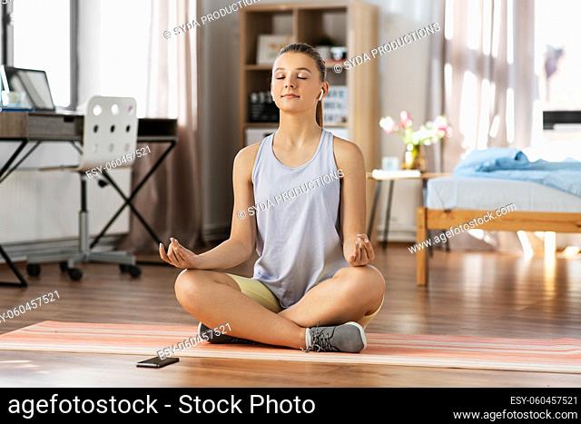 girl with phone and earphones meditating at home