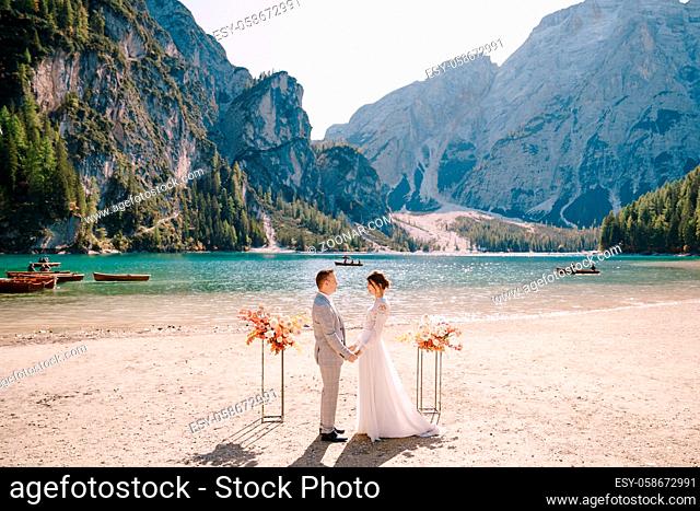 The groom dons a bride's ring, in place for the ceremony, with an arch of autumn floral columns, against the backdrop of Lago di Braies in Italy