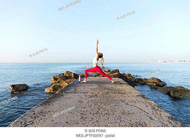 Young woman practicing yoga on the beach, doing warrior pose
