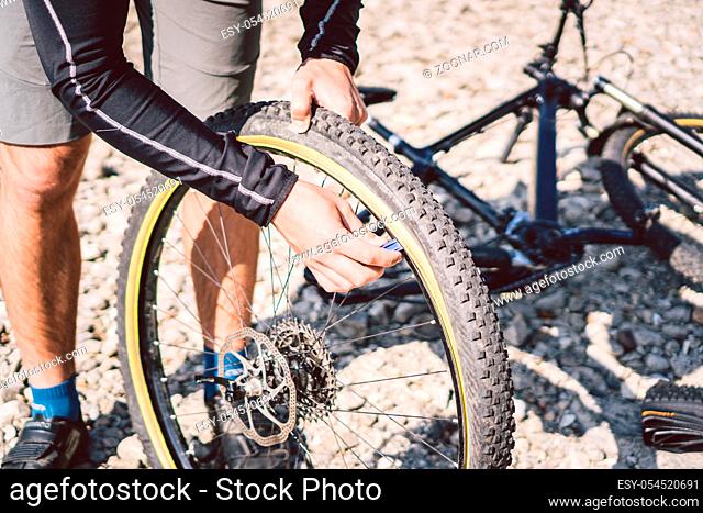 Bike Repair. Man Repairing Mountain Bike. Cyclist man in trouble rear wheel wheel case of accident. Man Fixes Bike near lake in Italy background mountains