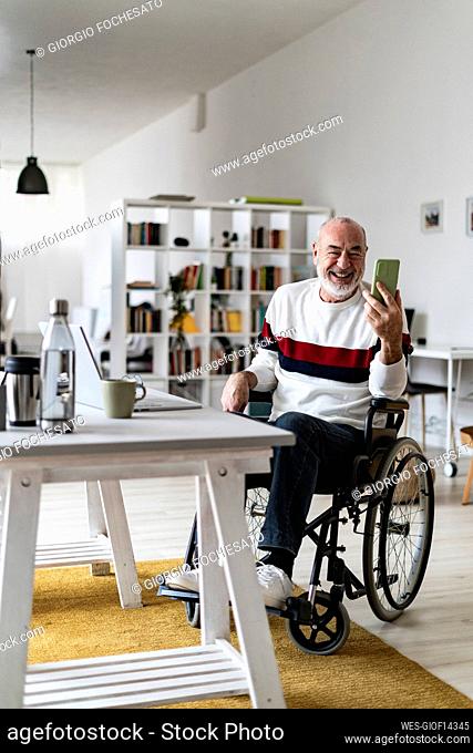 Businessman on wheelchair attending video call through mobile phone at home