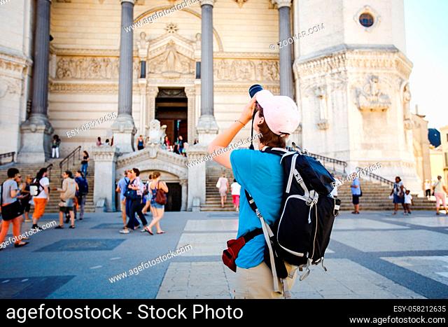 Bergamo Italy girl backpacker standing with backshot photo temple attractions. Dressed in a pink cap, a blue T-shirt and shorts behind a black backpack