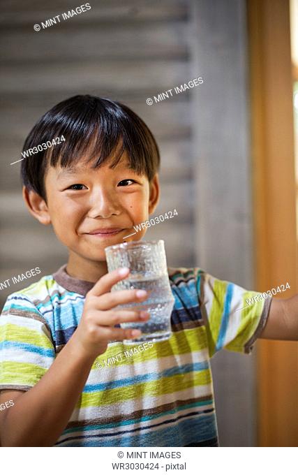 Portrait of boy with black hair wearing stripy T-shirt, holding drinking glass, smiling at camera