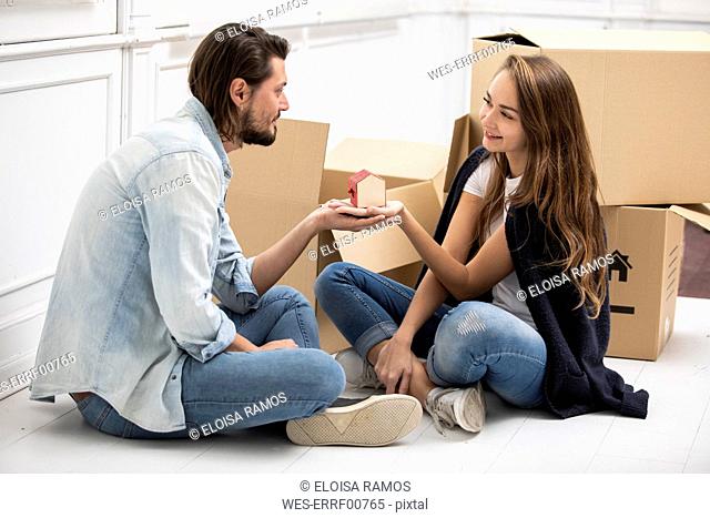 Man handing over tiny house model to girlfriend surrounded by cardboard boxes