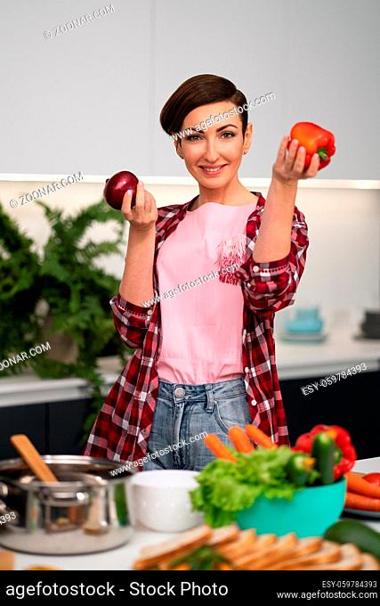 Holding apples in the hands housewife wearing plaid shirt with a short hairstyle while cooking apple pie standing at the kitchen. Healthy food at home
