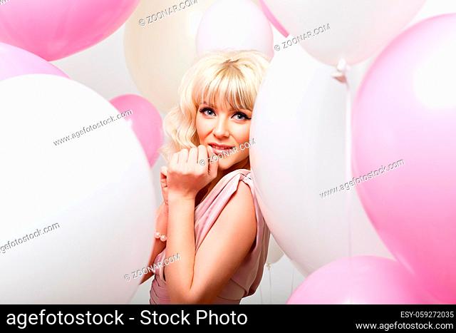 beautiful blonde young cheerful woman in long pink dress holding many air balloons. studio shot over white background. copy space